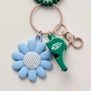 Close-up of blue silicone flower charm with green whistle and spring bracelet on keychain