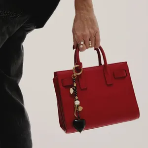 Detail of red leather handbag with black heart charm and decorative pearl keychain