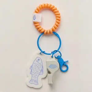 Close-up view of a cute fish and whistle bag charm featuring an orange spiral wristlet
