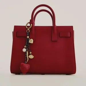 Detail of red leather handbag featuring heart-shaped charm and decorative pearl pendant