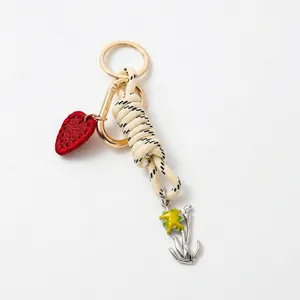 Detail of handmade braided rope keychain with red leather heart and floral metal charm