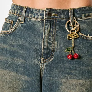 Cute cherry keychain with red fruit and gold chain hanging on vintage denim jeans pocket