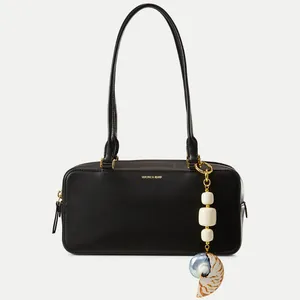 Detail der schwarzen Ledertasche mit Goldlogo und einem Muschel-Perlenanhänger
