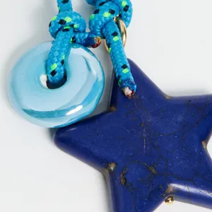 Close-up of ceramic heart and star pendant charm with blue braided cord and gold ring