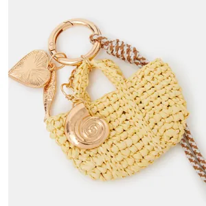 Detail of woven straw bag pendant with golden heart shell charms and nautical rope keychain