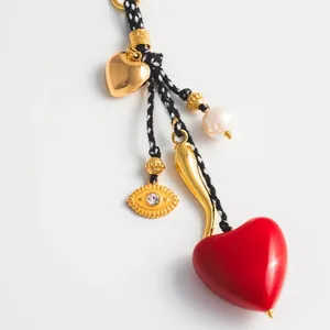 Detail of beaded bag charm with red heart, evil eye charm, and pearl on woven cord