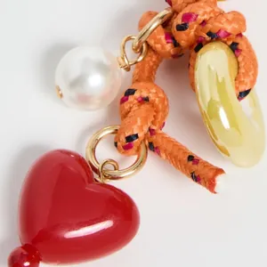 Close-up of woven orange cord bag charm with red heart, white pearl and acrylic ring