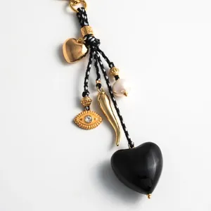Detail of a black heart charm pendant with gold eye and pearl on a braided rope cord