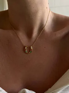 Close-up of horseshoe pendant with colorful crystals on a gold chain worn by a model