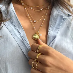 Detail van gelaagde gouden schelpenketting en parelringen voor een bohemien strandlook