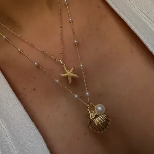Detail van de goudkleurige dubbellaagse ketting met schelp, zeester en parels