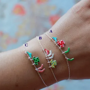 Colorful enamel boot and map charms on silver chain bracelets shown on a model
