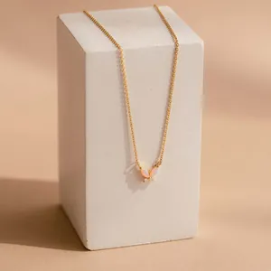Collana a farfalla dorata con ali di opale rosa su un supporto in pietra minimalista