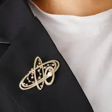 Detailed view of a gold-toned hollow planet brooch with pearl on a black suit lapel