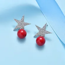 Macro detail of star-shaped zircon earrings with hanging red round pearls on blue silk