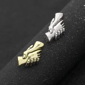 Dettaglio macro di spille a forma di mani in oro e argento su un supporto nero opaco