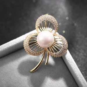 Dettaglio macro di spilla a fiore dorata con perla centrale e petali di zirconi