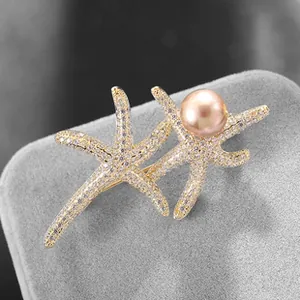 Vista macro di una spilla a stella marina dorata con diamanti e perla rosa chic