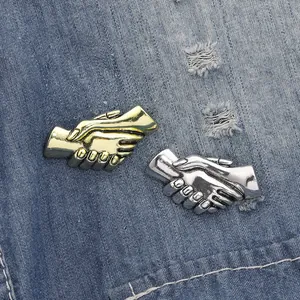 Dettaglio di spille vintage a forma di stretta di mano in oro e argento su jeans