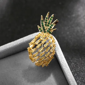 Broche de piña brillante con circones verdes y amarillos sobre joyero gris elegante