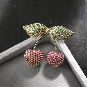 Dettaglio spilla a ciliegia con strass rossi e verdi e base in metallo dorato