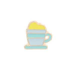 Dettaglio della spilla smaltata a forma di tazza di caffè con schiuma gialla e bordi oro