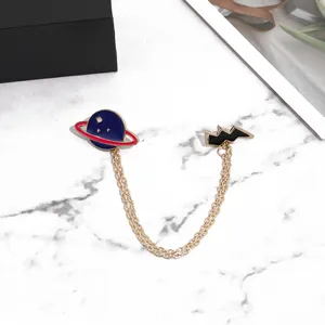 Détail de la broche à double chaîne avec planète bleue et éclair noir sur marbre