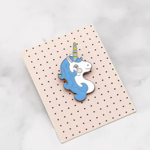 Dettaglio spilla unicorno bianco con criniera blu su cartoncino rosa a pois neri