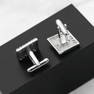 Detailed close-up of square silver cufflinks with textured finish on a dark marble stand