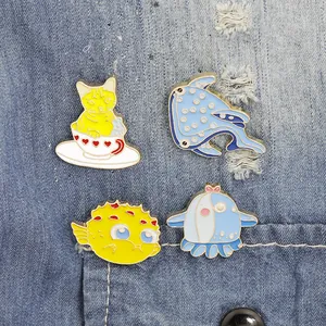 Cute cartoon cat and sea animal enamel pins displayed on blue denim fabric background