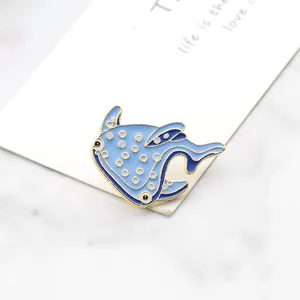 Detailed view of blue enamel whale brooch with gold accents on minimalist marble card