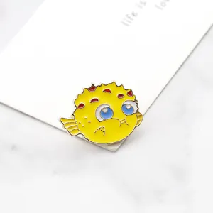 Detailed close-up of a yellow pufferfish enamel pin with red spots and golden edges