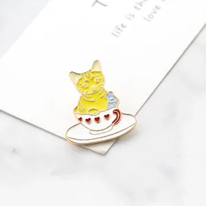 Detail of a cute yellow tabby cat enamel pin in a white coffee cup on a marble background