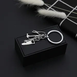 Detail shot of mini metal tool keychain featuring pliers, hammer, wrench, and saw on box