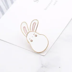 Détail macro d'une broche lapin en émail blanc avec bords dorés et touches de rose