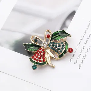 Detailed macro of gold Christmas bell brooch with red rhinestones and green enamel leaf