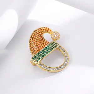 Golden Christmas hat brooch with vibrant orange and green zircons on white background