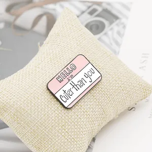Close-up of pink enamel 'Cuter than you' name tag brooch pin on a linen cloth background