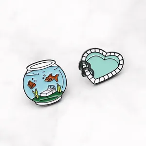 Broches en émail bocal à poisson et piscine cœur sur fond de marbre blanc