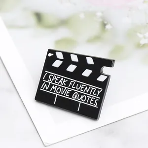 Dettaglio macro della spilla smaltata a ciak con testo I Speak Fluently in Movie Quotes