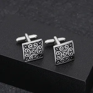 Detailed macro view of square silver cufflinks with intricate scroll patterns in a gift box