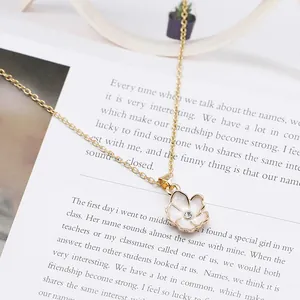 Dettaglio di una collana dorata con pendente a fiore in smalto bianco e zircone centrale