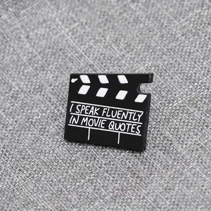 Dettaglio della spilla in smalto a forma di ciak cinematografico con citazione di film