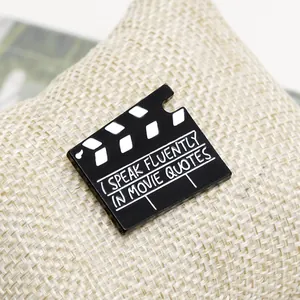 Spilla smaltata vintage a forma di ciak con citazione cinematografica su sfondo di iuta grezza