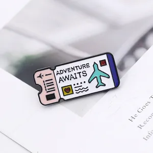 Detail of enamel boarding pass brooch with Adventure Awaits text on magazine background