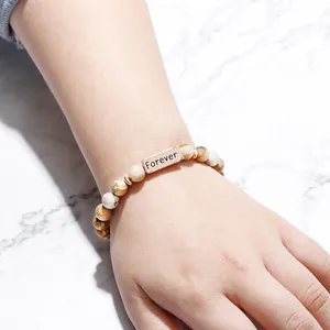 Detail van natuursteen kralenarmband met een roségouden Forever gegraveerd metalen plaatje