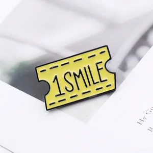 Close-up of yellow enamel ticket brooch with 1 SMILE text and black drip oil details
