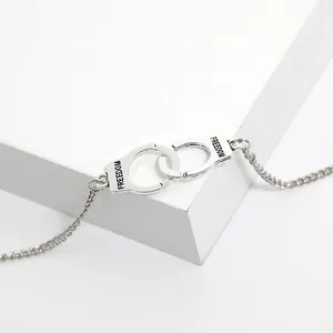 Detail shot of silver handcuff charm featuring freedom engraving on a minimalist chain