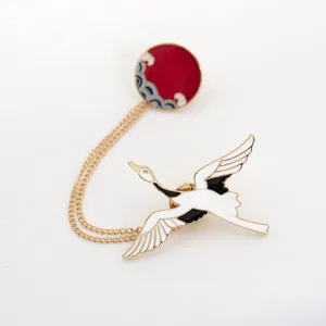 Detailed view of enamel crane brooch with sun pattern and elegant gold chain link