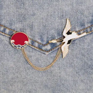 Detail of cartoon crane enamel pin with red sun and wave charms on denim jacket